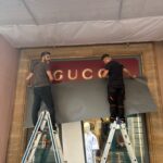 Operatori di Raia srl applicano gli sticker all'insegna del negozio Gucci.