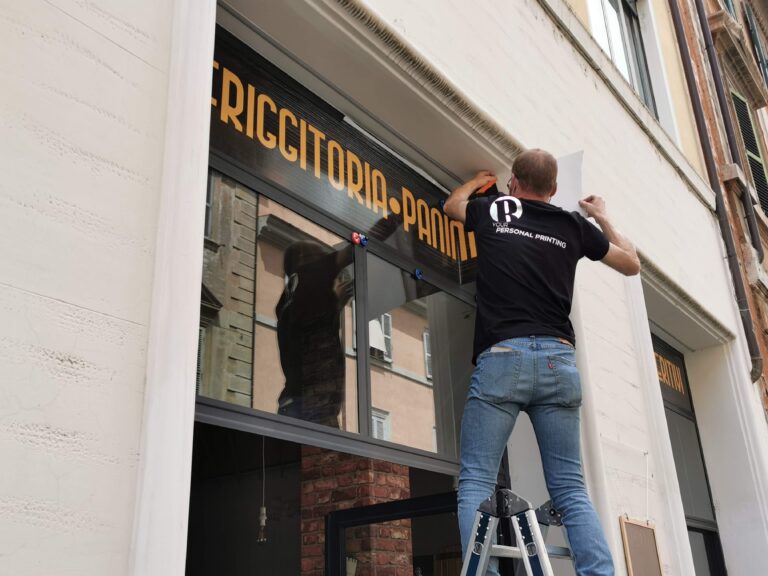 Operatore della Raia srl applica adesivo all'entrata di un negozio.