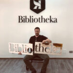 Sul muro l'insegna di Bibliotheka mentre l'operatore di Raia srl tiene le matrici.