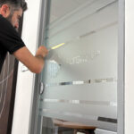 Operatore di Raia srl applica la vetrofania ad una porta di vetro.